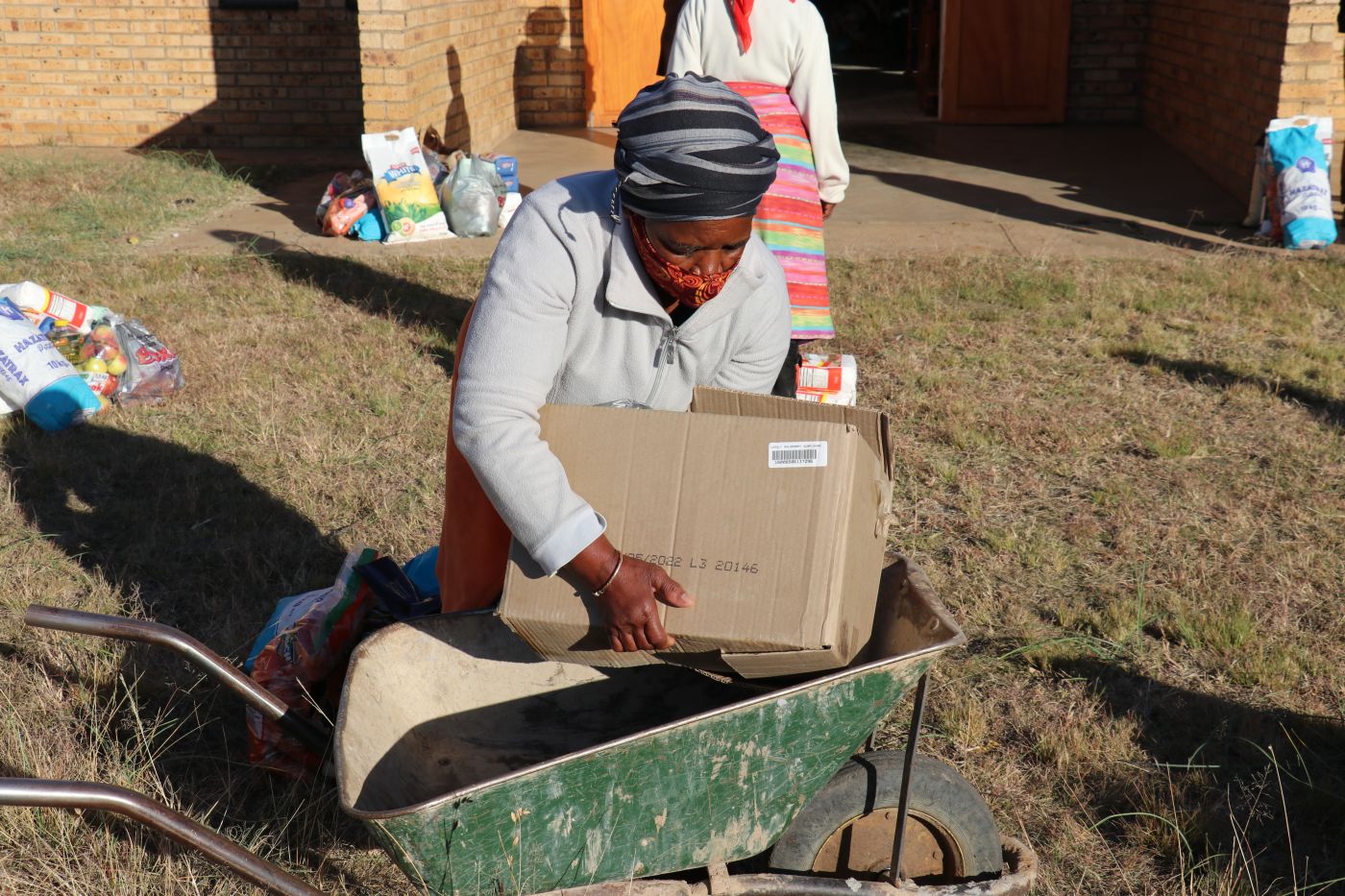 A woman loads a wheelbarrow at an E1 F1 food distribution at Bodibe